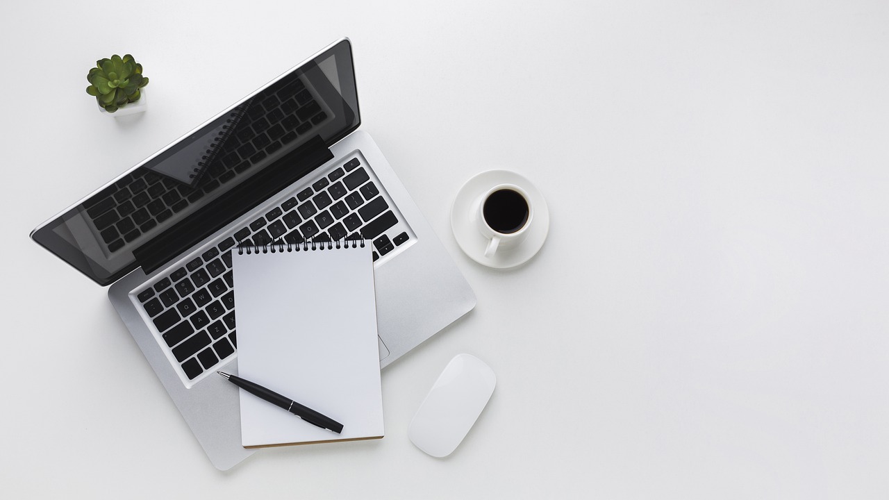 A clear desk with a laptop, notebook, and coffee